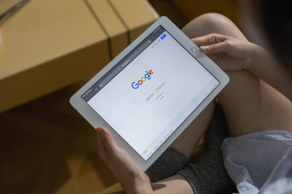 THE GOOGLE INTERFACE IS SHOWN IN A WHITE TABLET HOLDING IN THE HAND